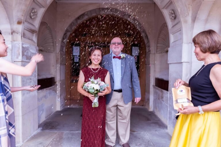 Couple in an ornate stone archway, the bride in a red dress holding a bouquet
