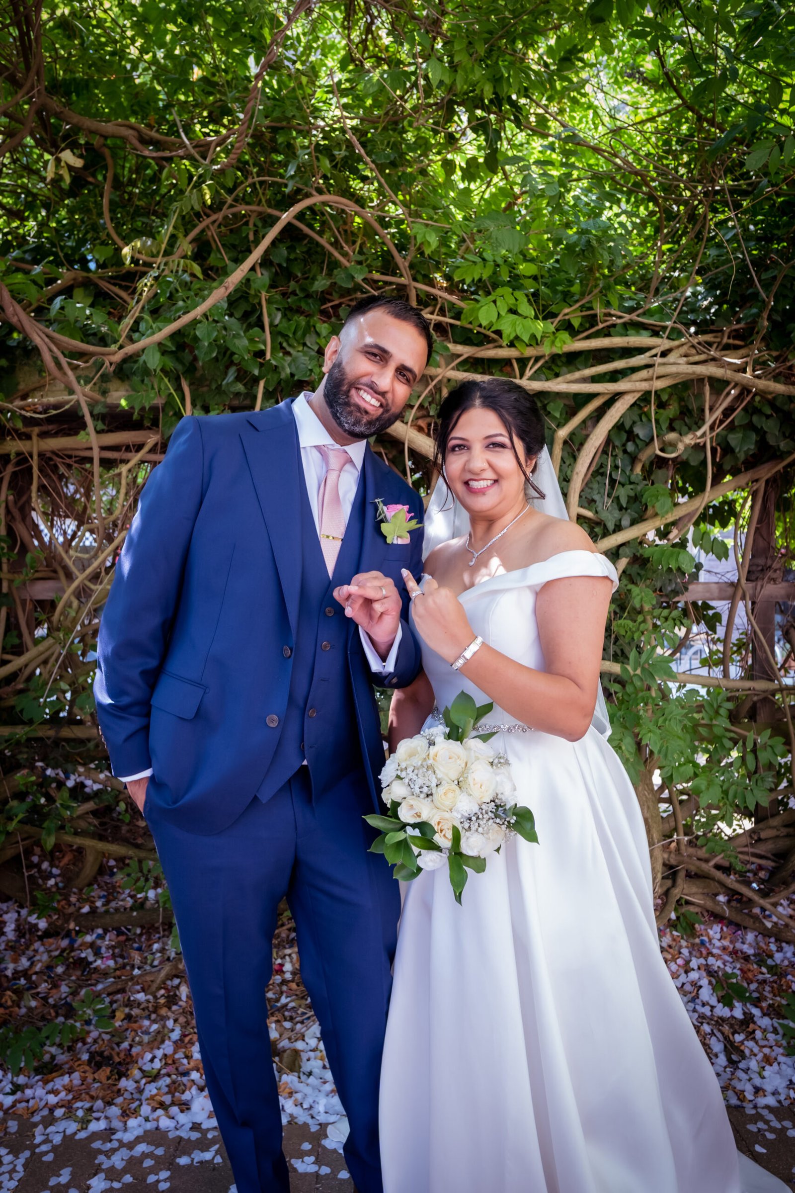 Bride in a white gown and groom in a blue suit posing outdoors among trees