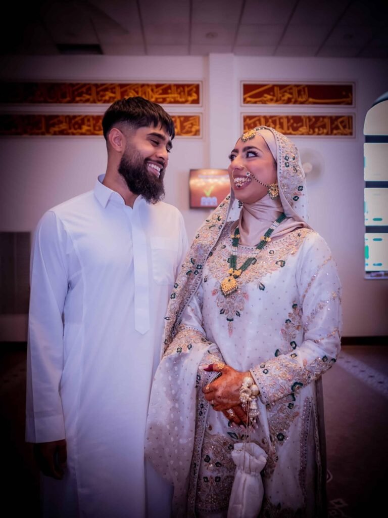 Couple in white embroidered wedding outfits smiling at each other
