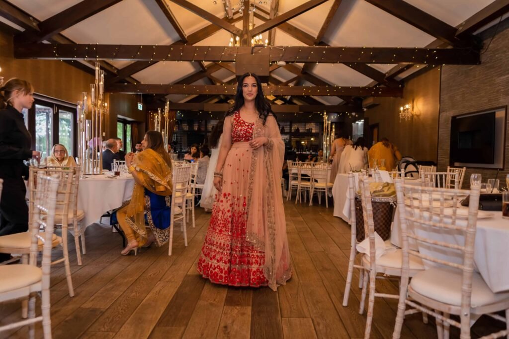 Bride in a red and gold lehenga standing in a beamed reception venue