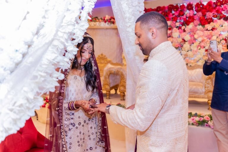 Seated couple exchange rings amid warm floral du00e9cor during an Asian wedding ceremony