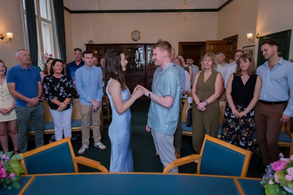 Couple hold hands encircled by standing guests during a civil wedding ceremony