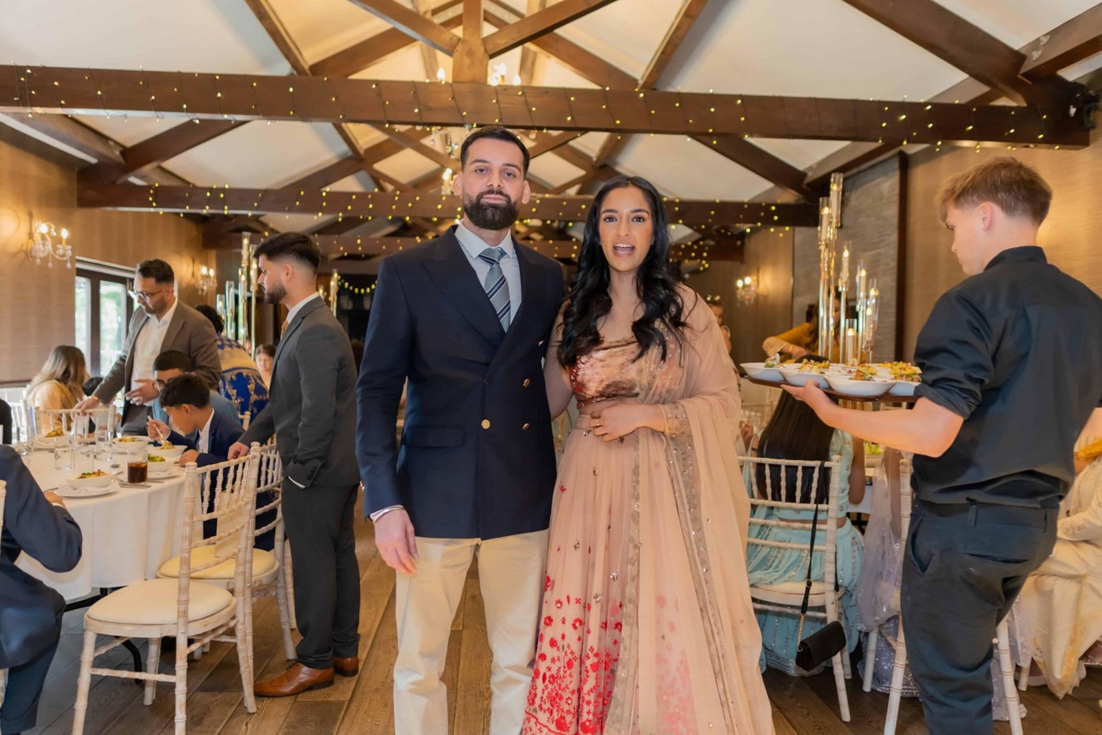 Family and guests gathered in a beamed barn reception, the bride in red