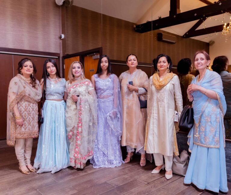 Women guests in elegant pastel South Asian outfits posing together
