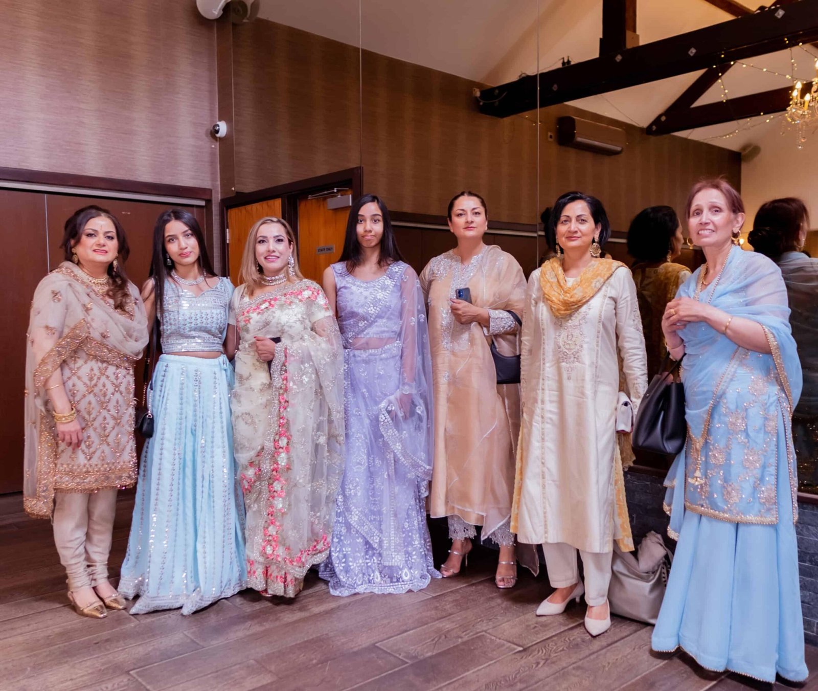 Women guests in elegant pastel South Asian outfits posing together