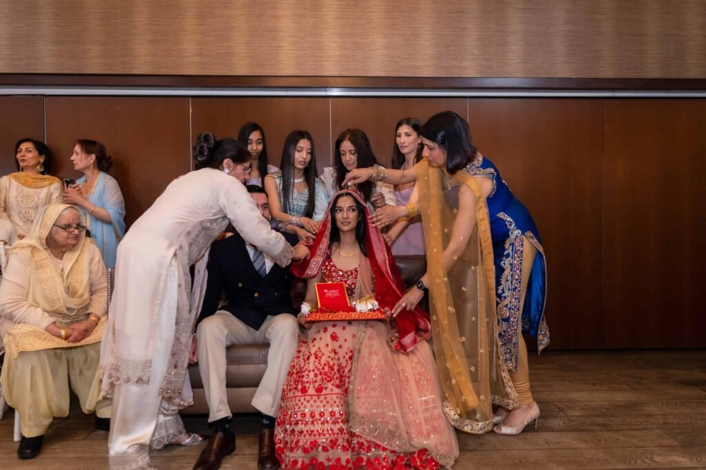 Bride in a red and gold lehenga seated with family during an Asian wedding ceremony