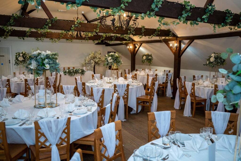 Barn reception set with round tables, white linen and fairy lights under wooden beams