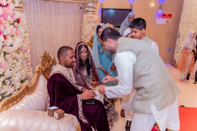 Seated couple exchange rings during an Asian wedding ceremony with family close by