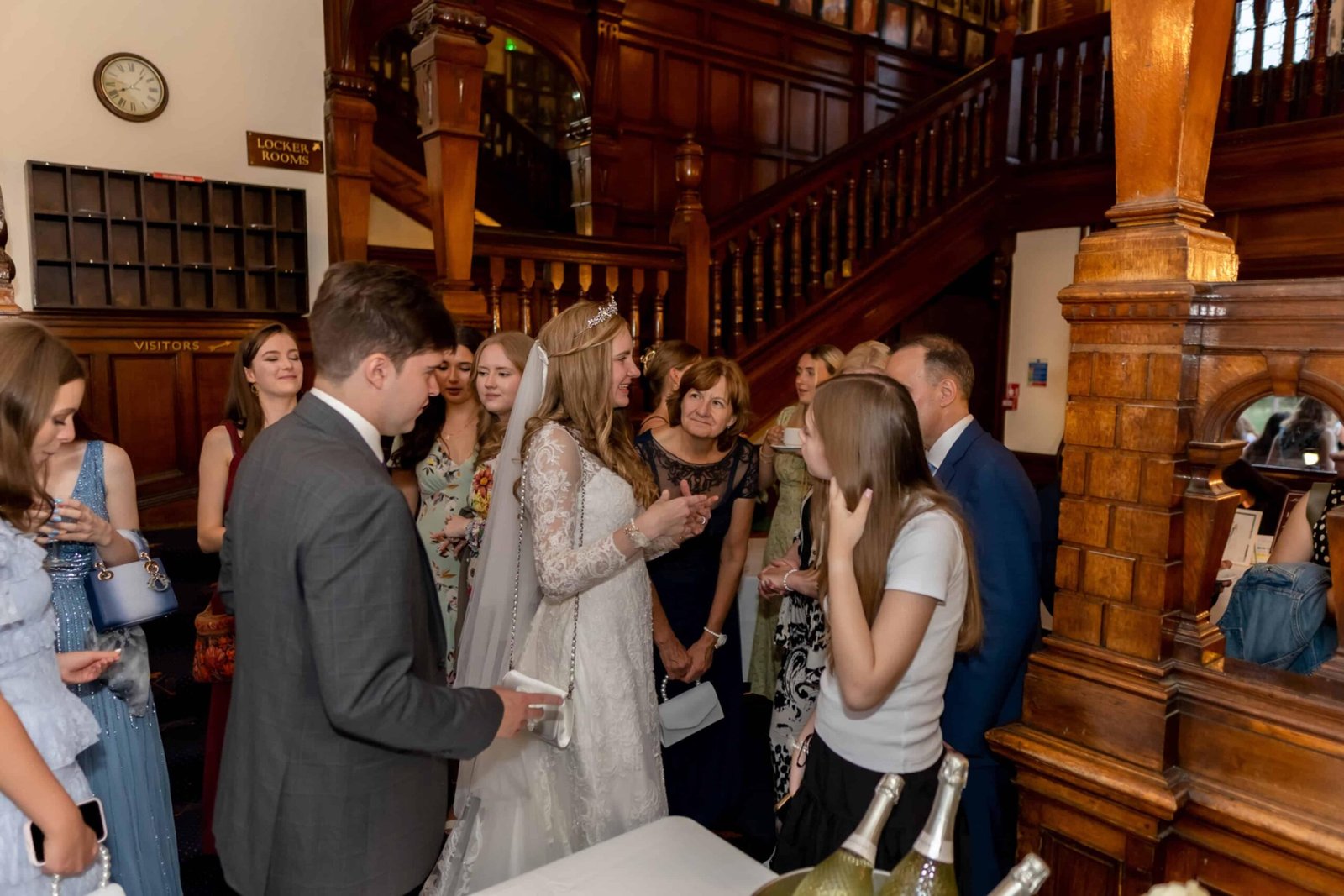 Guests at a drinks reception beside a grand carved wooden staircase
