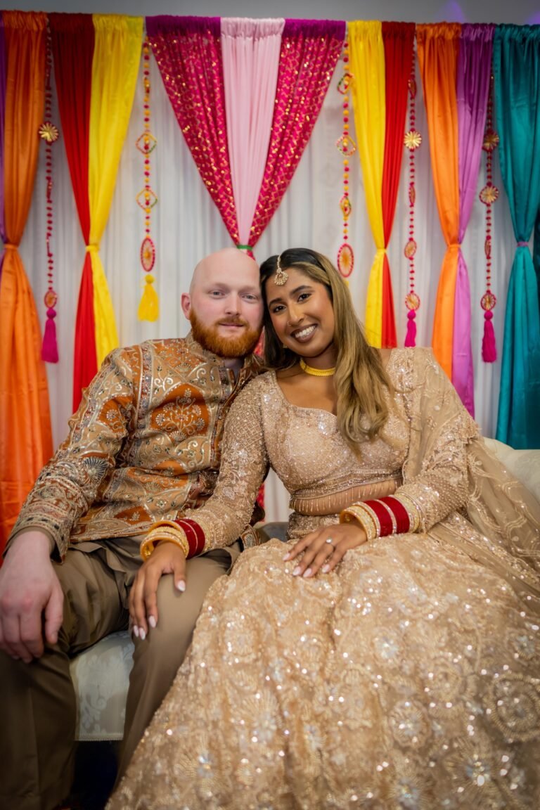 Couple in gold attire embrace against a colourful draped backdrop