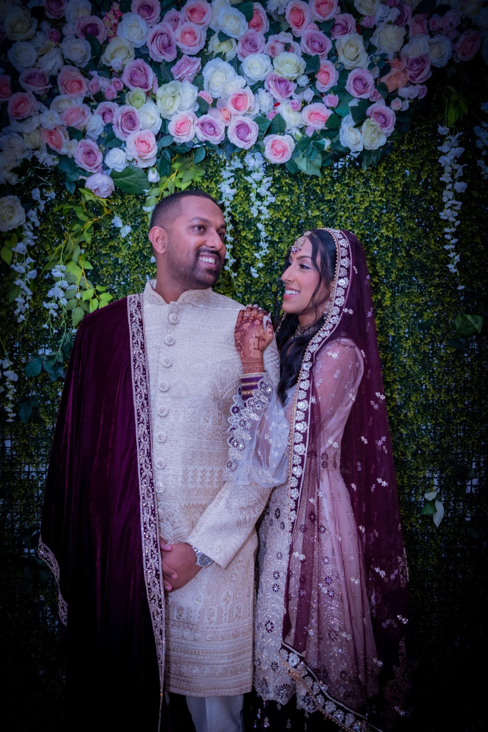 Couple at a greenery and floral arch, the groom in a cream sherwani – Asian wedding photographer